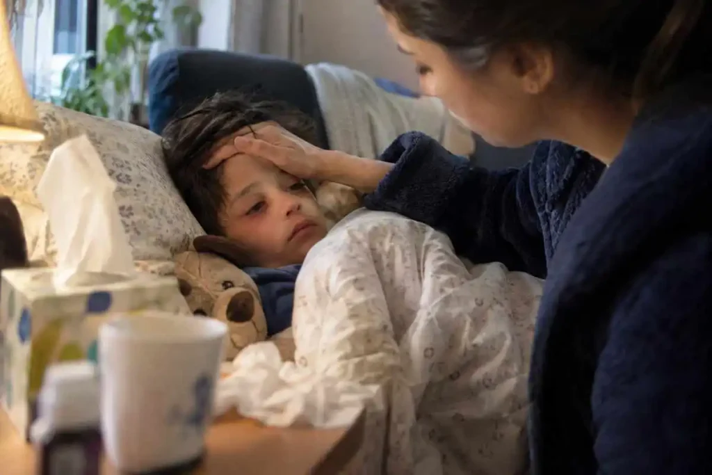 Sick child resting in bed while a mother checks his forehead at home