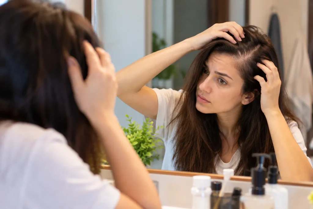 Woman examining her hair part in a bathroom mirror